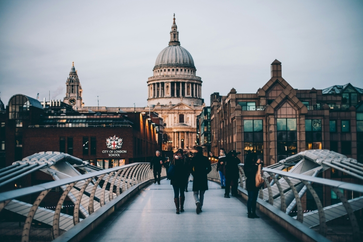 People walking on the Millennium Bridge in London, with St. Paul's Cathedral and the City of London School in the background. 