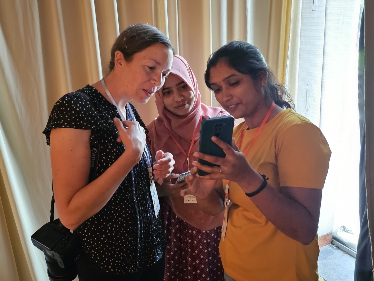 Three women look at a smartphone.