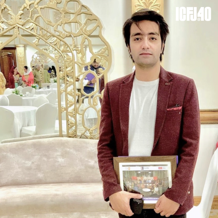 A photo of Shahzad Naveed standing in an elegant banquet room. He's holding a framed photo.