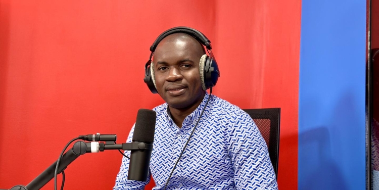 Facely Konaté wears headphones and sits in front of a radio microphone.