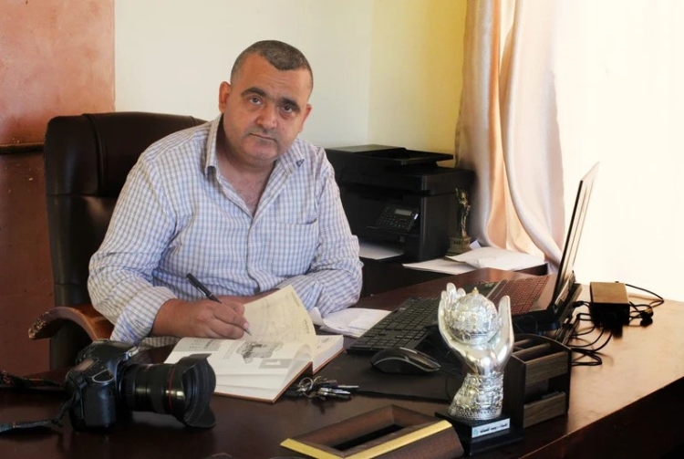 A photo of Naaman Ashtawy from APA Images. He's sitting at a desk and writing in a book.