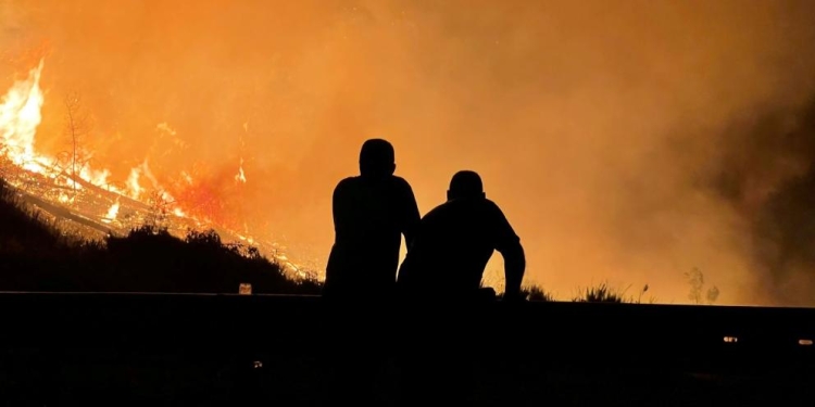 A photo of two people silhouetted against a wildfire. 