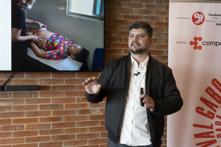 A photo of Daniel Nardin speaking in front of a TV screen. The screen displays an image of a woman receiving an ultrasound.