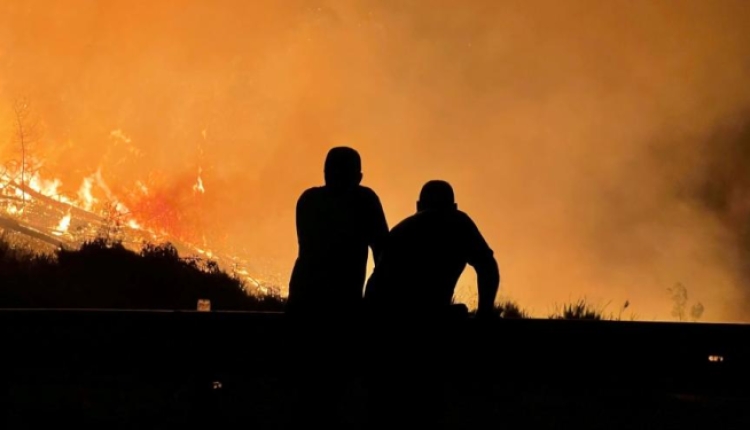 A photo of two people silhouetted against a wildfire. 